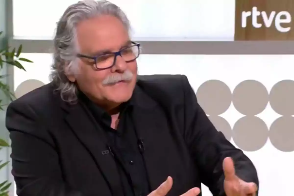 Un hombre con cabello canoso y gafas está hablando en un estudio de televisión.