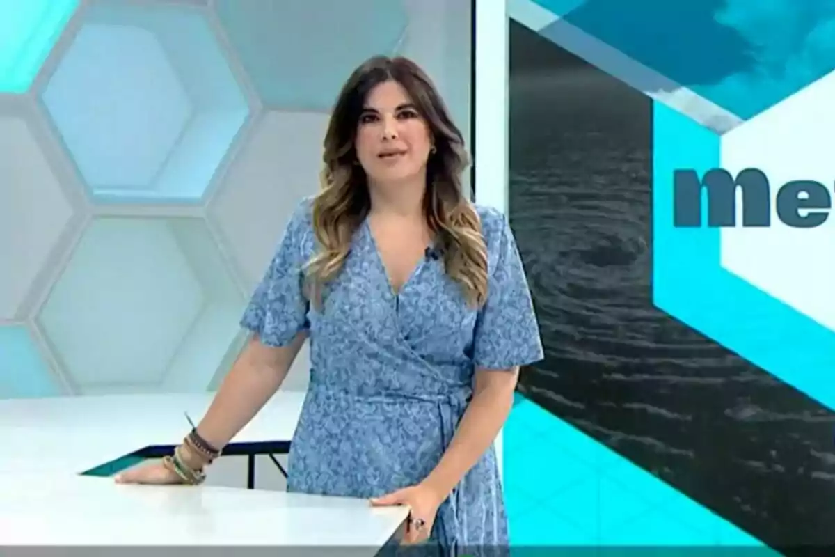 Joanna Ivars dempeus en un estudi de televisió amb un vestit blau i fons geomètric. Joanna Ivars dempeus en un estudi de televisió amb un vestit blau i fons geomètric.