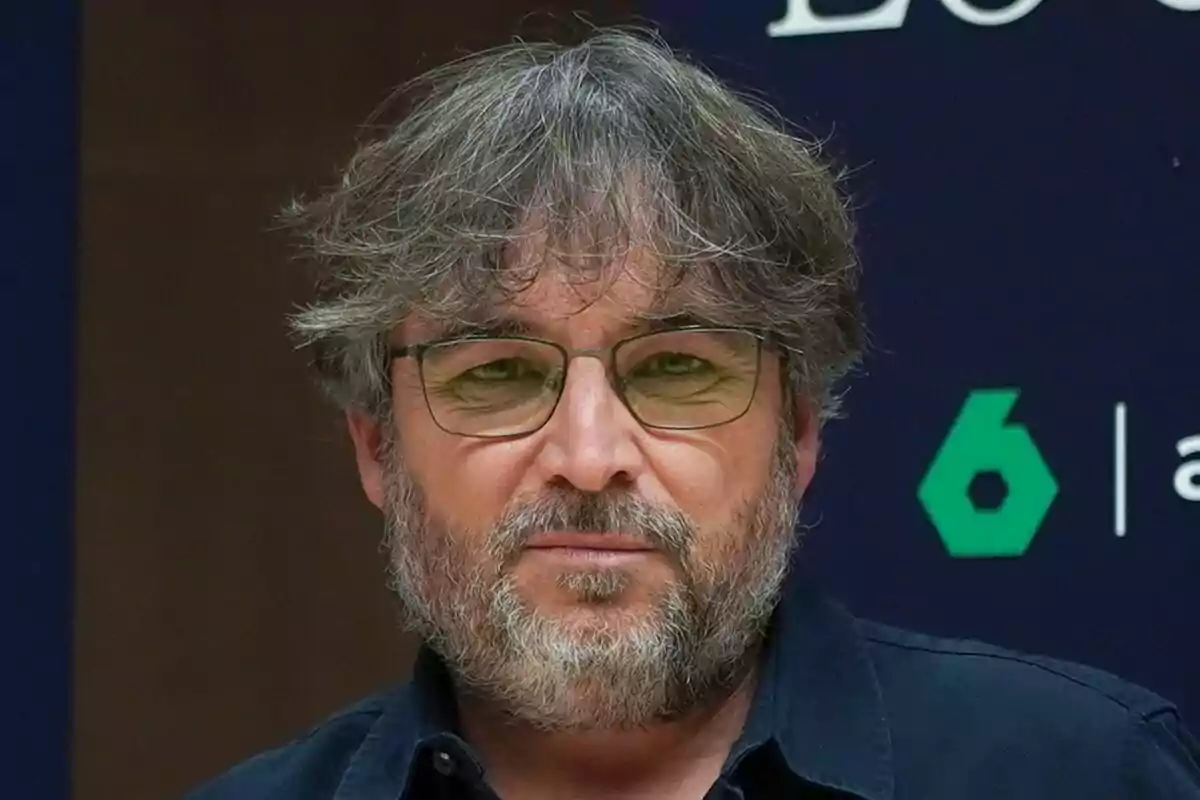 Jordi Évole con barba y gafas, de cabello canoso y despeinado, viste una camisa oscura frente a un fondo con texto y logotipos de Lo de Évole y laSexta.