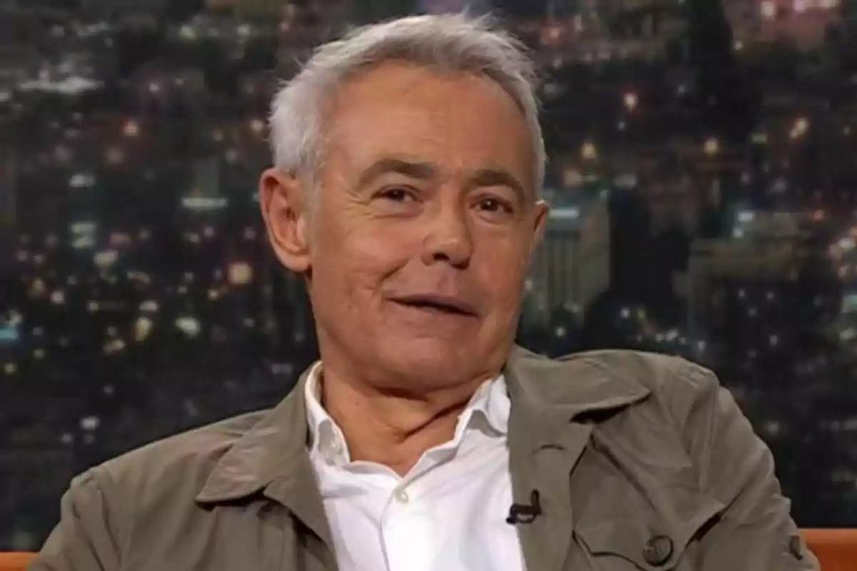 Jordi González de cabell canós i curt amb jaqueta beix i camisa blanca assegut en un plató de televisió de Col·lapse amb fons de ciutat desenfocat