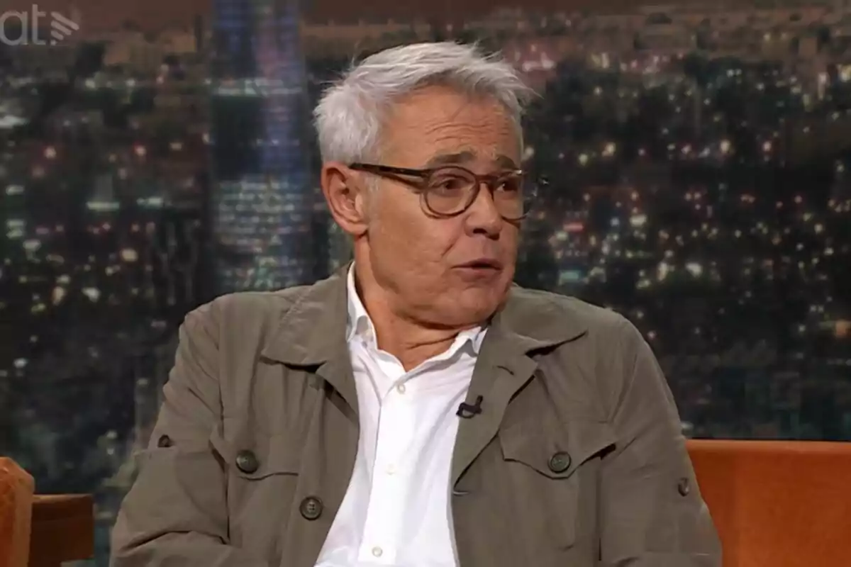 Jordi González de cabells canosos i ulleres assegut en un plató de televisió de Col·lapse amb fons de ciutat il·luminada