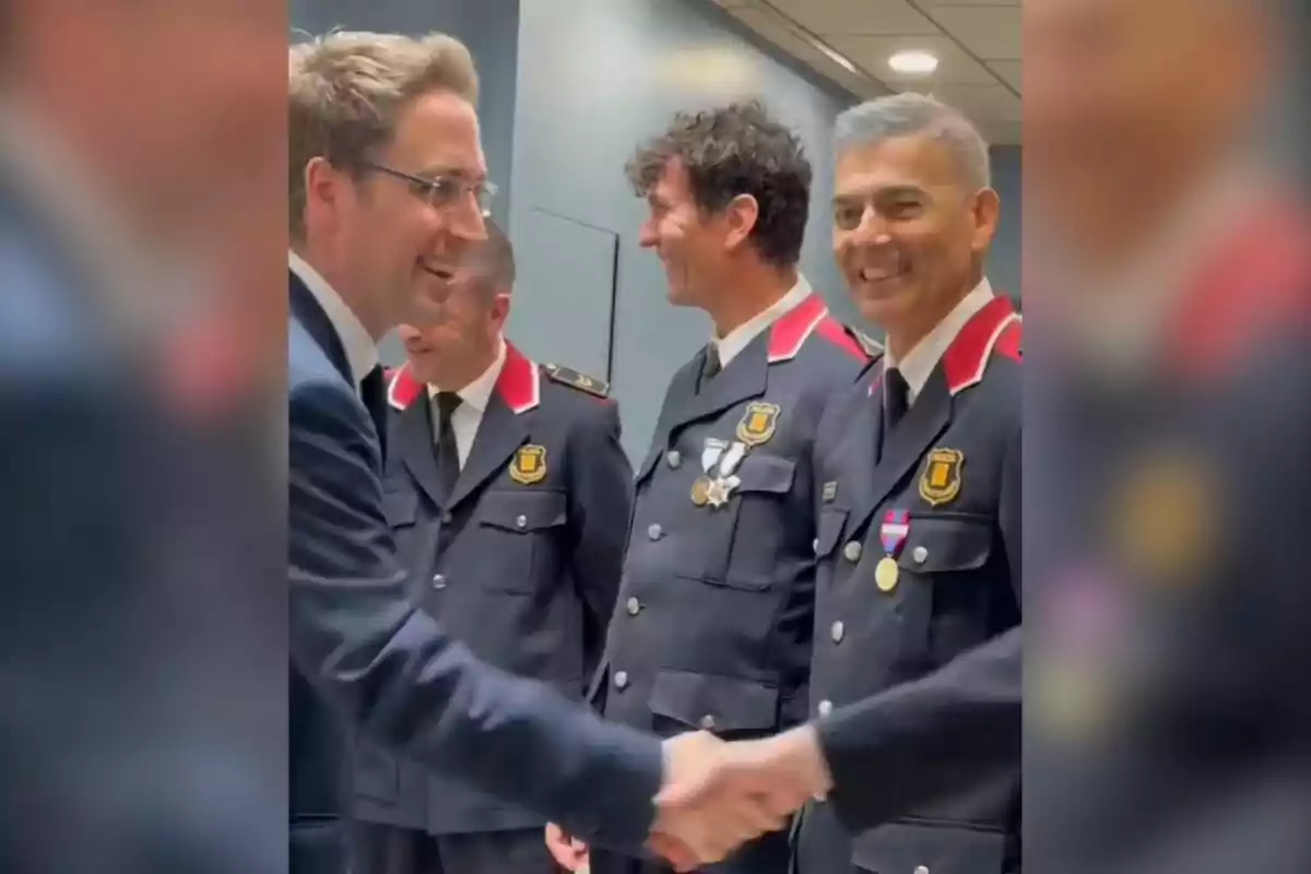Un grup de persones amb uniforme de policia somriu mentre una d'elles dona la mà a un home amb vestit. Un grup de persones amb uniforme de policia somriu mentre una d'elles dona la mà a un home amb vestit.