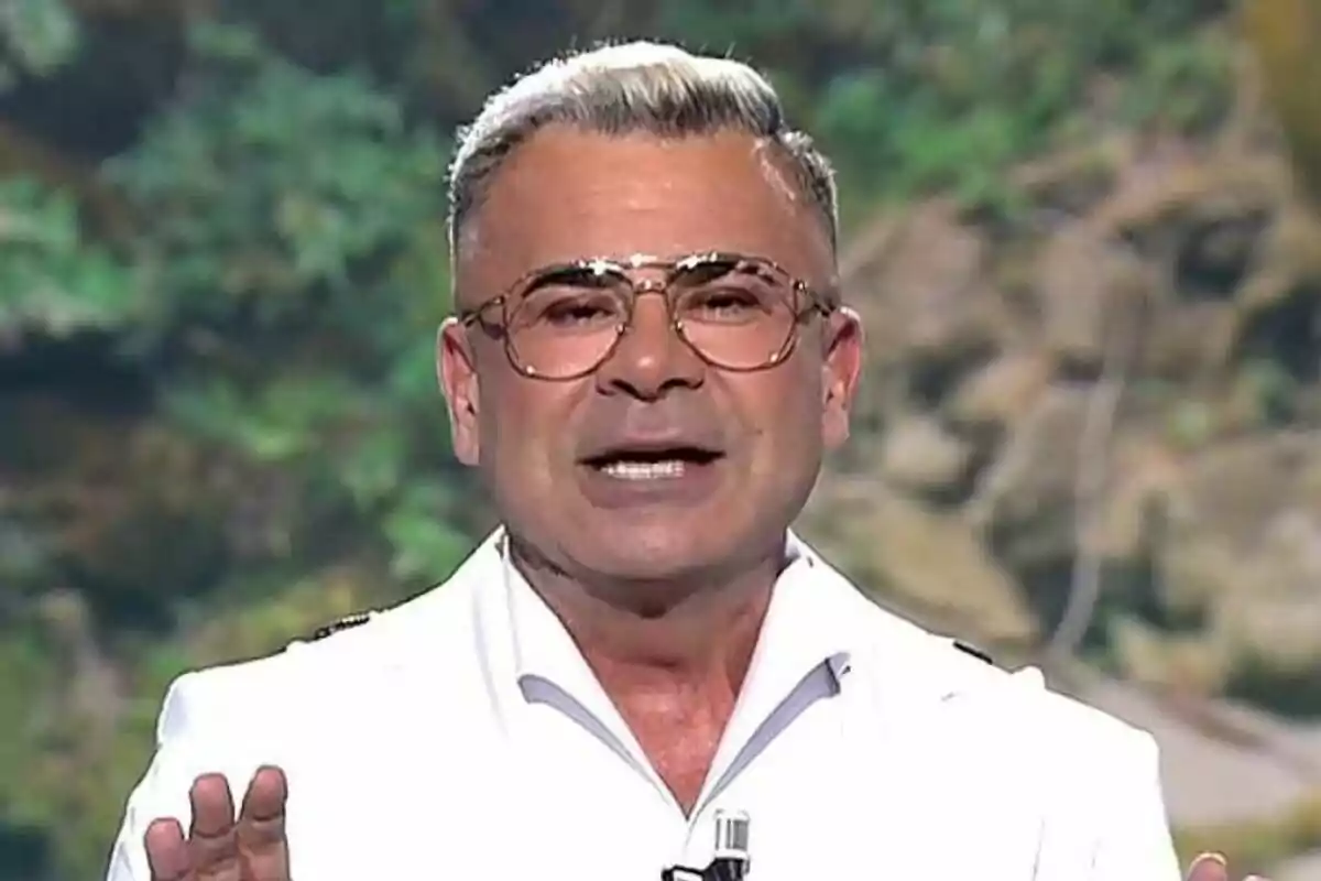 Jorge Javier Vázquez con gafas y cabello corto canoso viste una camisa blanca frente a un fondo natural en Supervivientes.