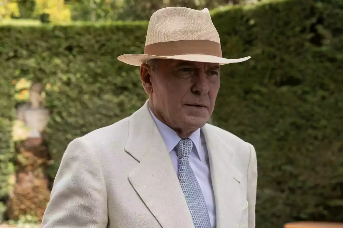 José Coronado amb barret de palla i vestit clar en un jardí a El Problema Final.