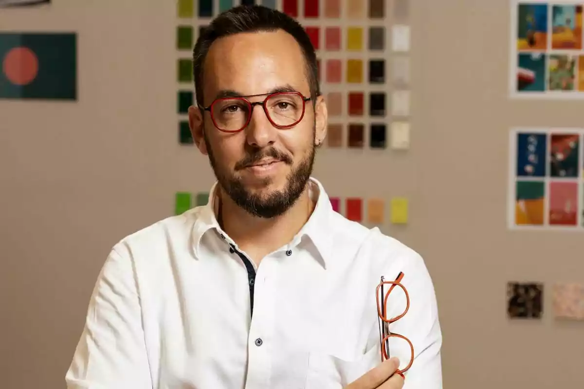 Josep Dosta, CEO de Woodys Eyewear, amb ulleres vermelles i camisa blanca sosté un parell d'ulleres en una mà davant d'una paret amb mostres de colors. Josep Dosta, CEO de Woodys Eyewear, amb ulleres vermelles i camisa blanca sosté un parell d'ulleres en una mà davant d'una paret amb mostres de colors.