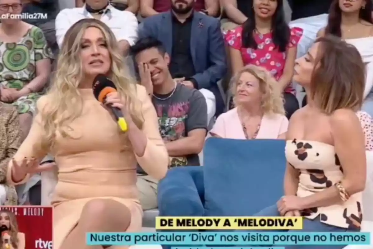 La imitació de Melody i María Patiño conversen a 'La família de la tele' amb públic al fons, una d'elles sosté un micròfon i l'altra l'observa atentament mentre diverses persones del públic somriuen. La imitació de Melody i María Patiño conversen a 'La família de la tele' amb públic al fons, una d'elles sosté un micròfon i l'altra l'observa atentament mentre diverses persones del públic somriuen.