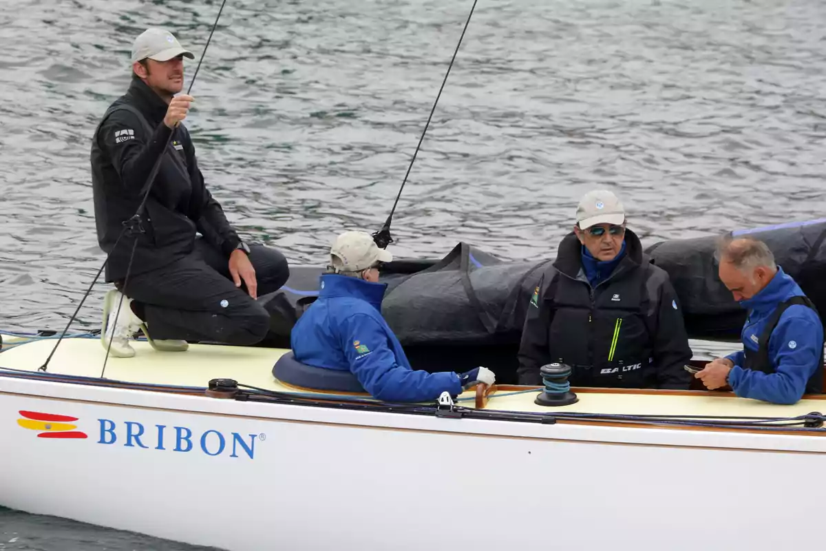 A group of people wearing warm clothes and caps is on a sailboat called Bribon on the water. A group of people wearing warm clothes and caps is on a sailboat called Bribon on the water.