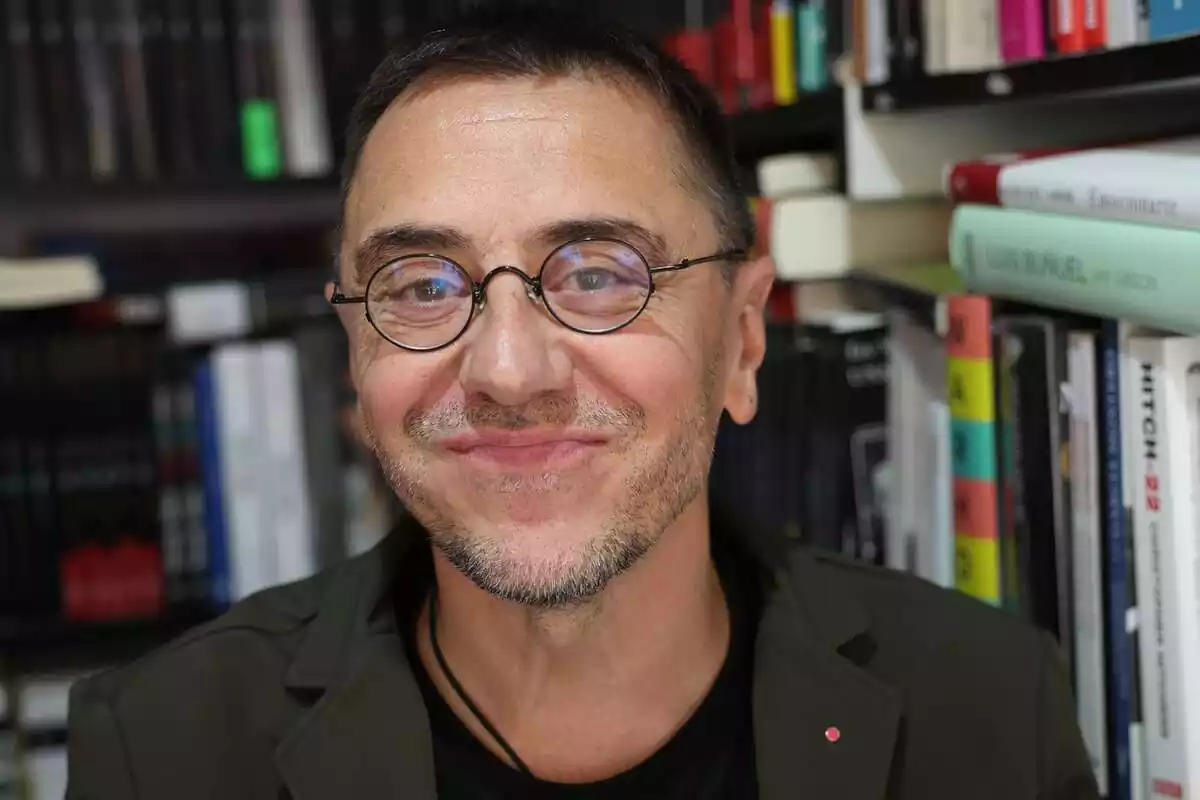 Primer pla de Juan Carlos Monedero somrient i de fons una prestatgeria amb llibres