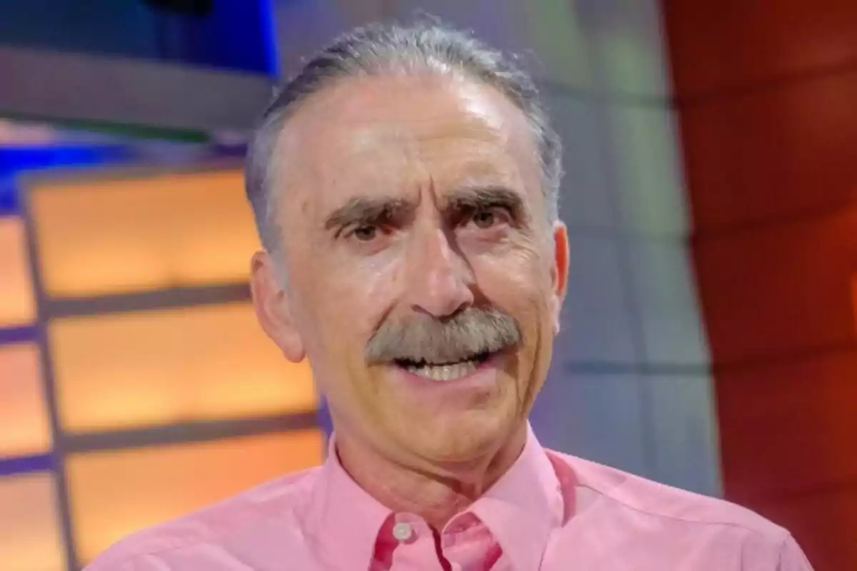 Juan y Medio de cabell canós i bigoti somriu mentre porta una camisa rosa en un entorn amb llums càlides a La tarda, aquí i ara.