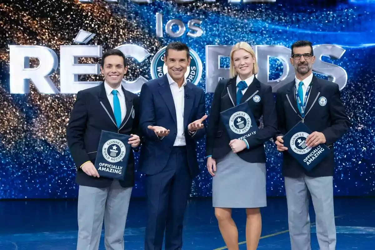 Els jutges i Jesús Vázquez posant en un escenari amb el logotip de Guinness World Records al fons, tots vestits amb vestits formals i somrient a la càmera. Els jutges i Jesús Vázquez posant en un escenari amb el logotip de Guinness World Records al fons, tots vestits amb vestits formals i somrient a la càmera.