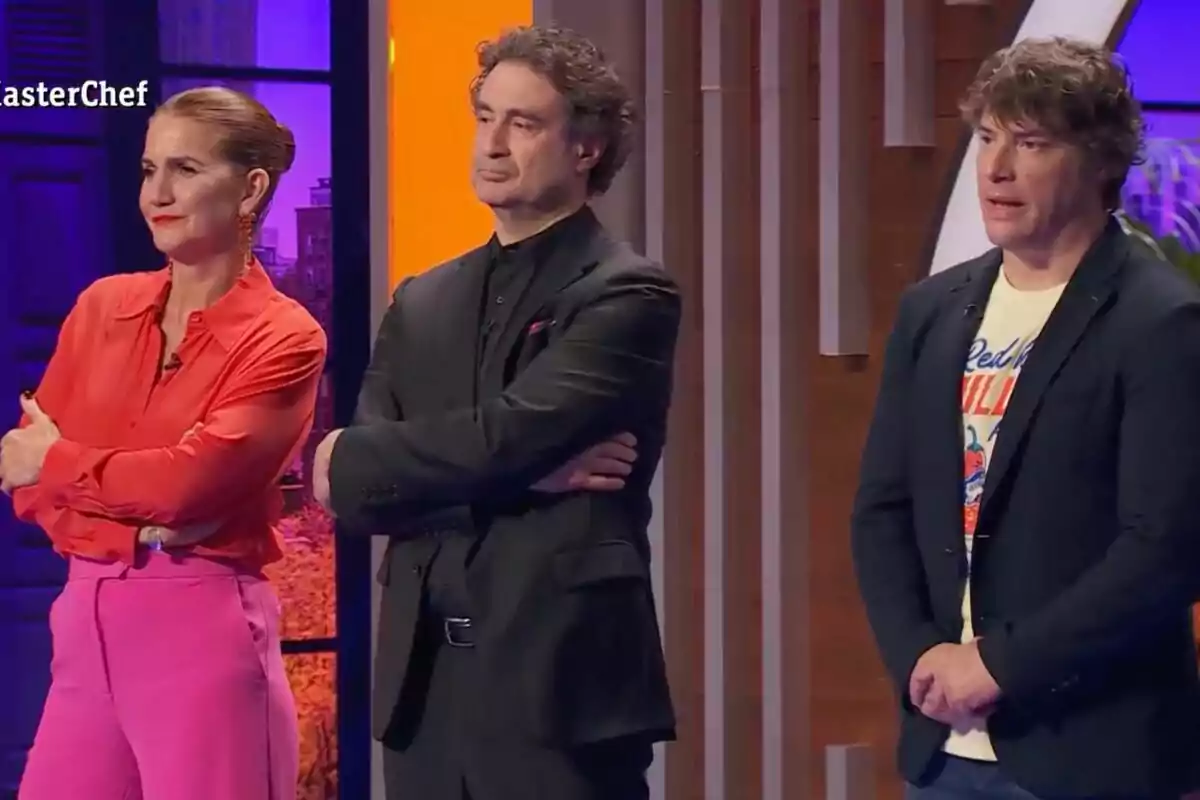 El jurat de 'Masterchef' dret amb expressions serioses en un plató de televisió il·luminat amb llums de colors.