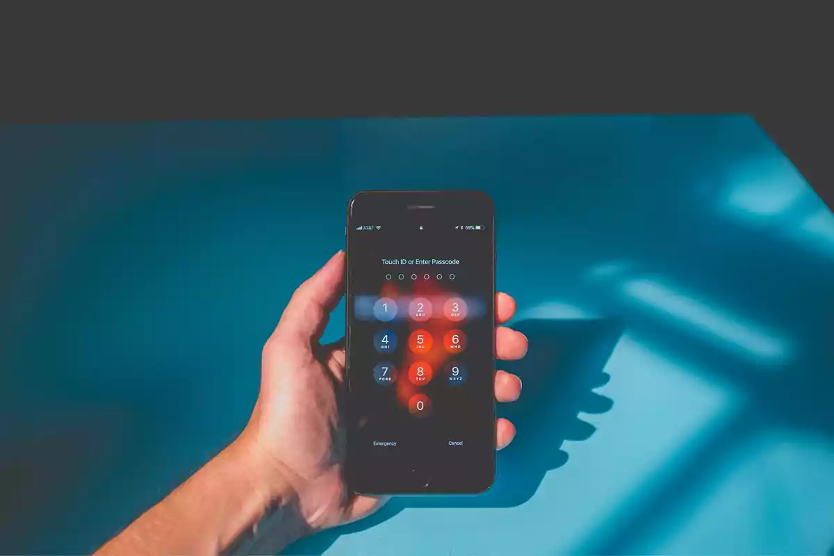 Una mano sosteniendo un teléfono inteligente con la pantalla de ingreso de código de acceso iluminada.