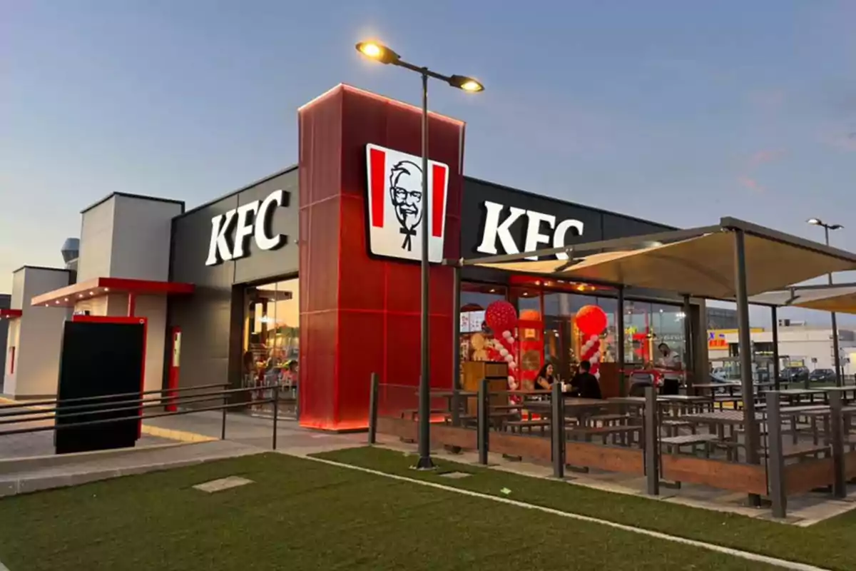 Franquicia de comida rápida KFC con área de comedor al aire libre y decoración de globos rojos y blancos.