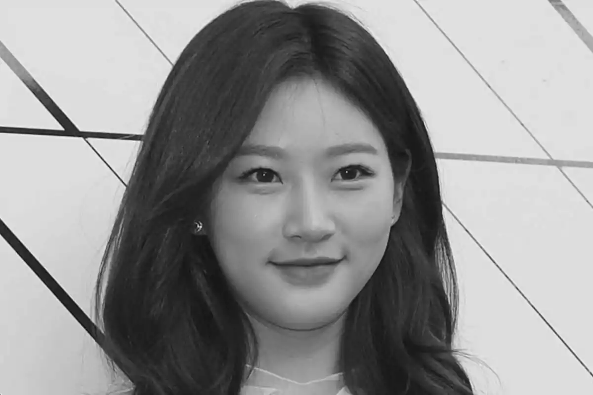 Kim Sae-ron con cabello largo y oscuro sonriendo frente a un fondo con líneas diagonales en una fotografía en blanco y negro.