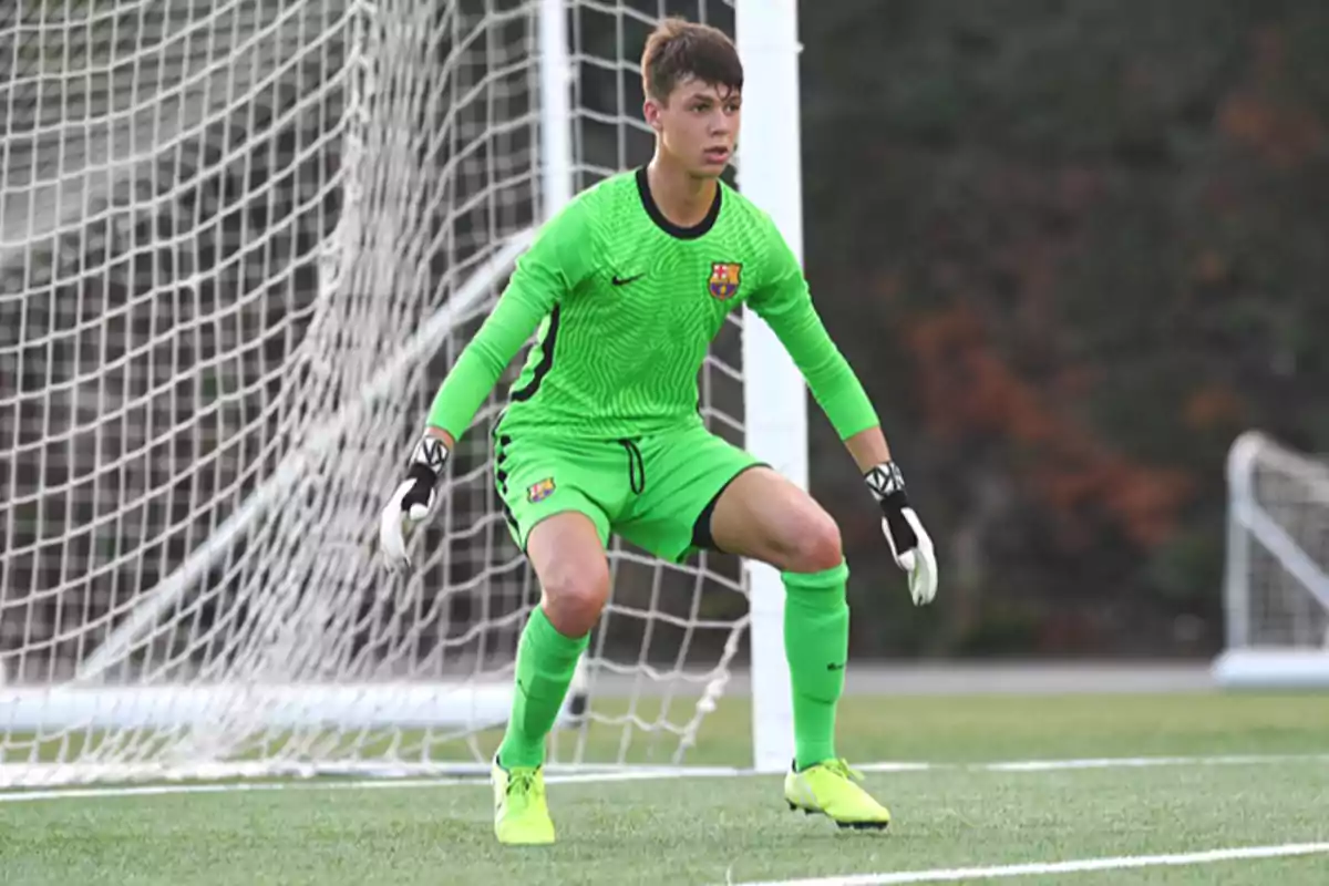 Joven portero con uniforme verde en posición de defensa frente a la portería en un campo de fútbol. Joven portero con uniforme verde en posición de defensa frente a la portería en un campo de fútbol.