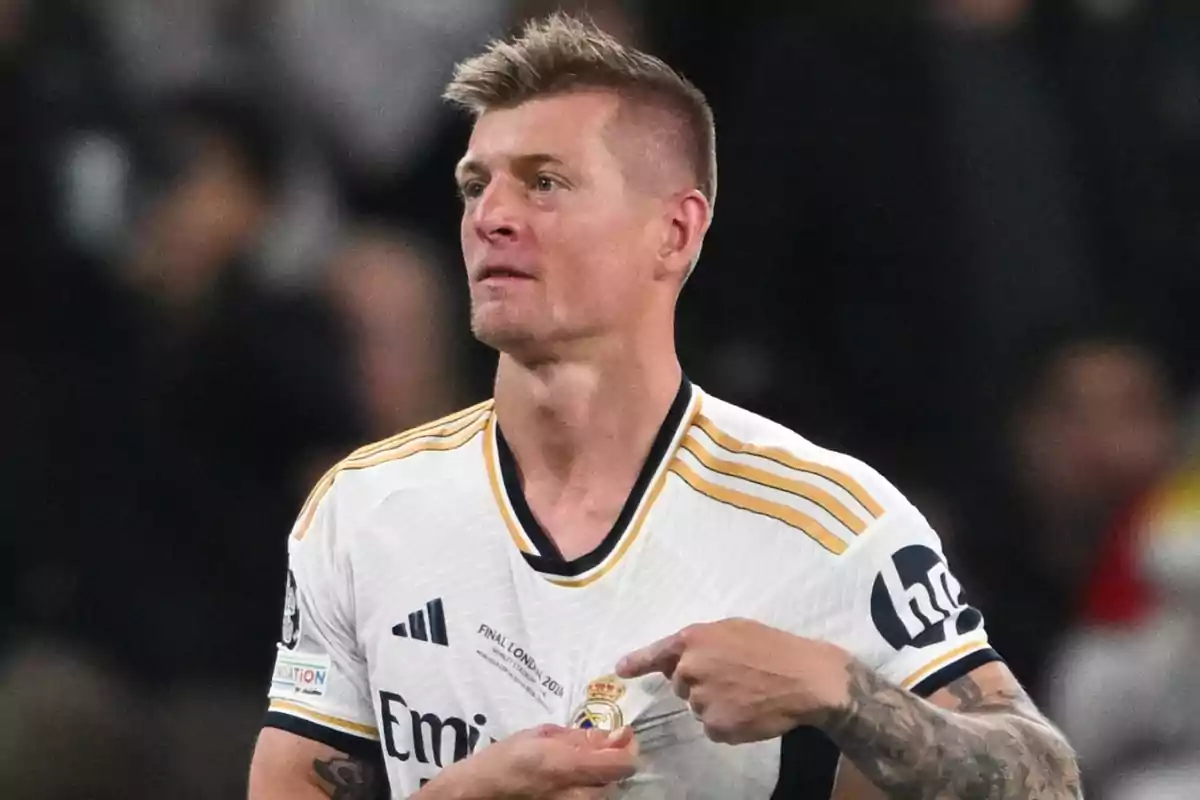 A soccer player wearing a Real Madrid shirt pointing to the team's shield.