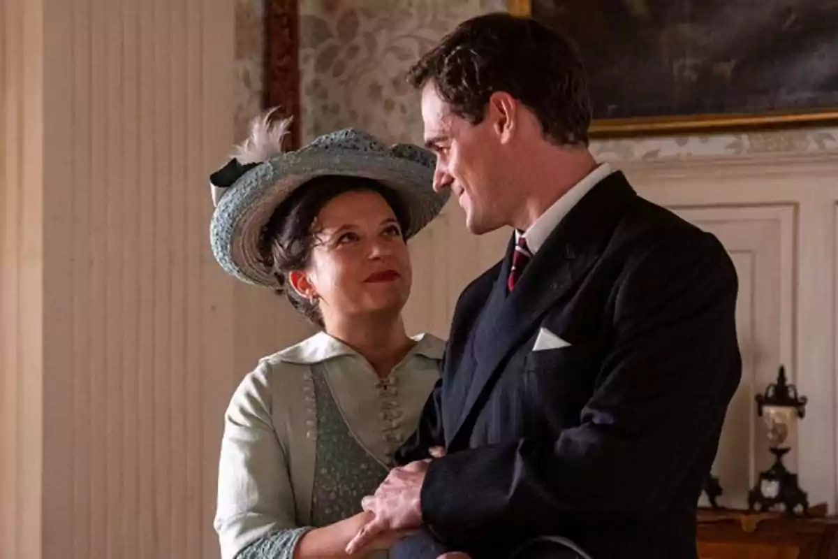 Martina and Jacobo dressed in vintage clothes is seen with affection in an elegantly decorated room. Capture of 'the promise'