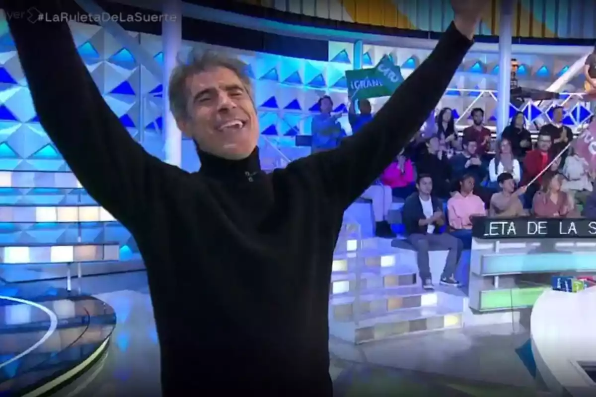 Jorge Fernández con suéter negro levanta los brazos en un plató de televisión con público en el fondo. Captura de 'La Ruleta de la Suerte' Jorge Fernández con suéter negro levanta los brazos en un plató de televisión con público en el fondo. Captura de 'La Ruleta de la Suerte'