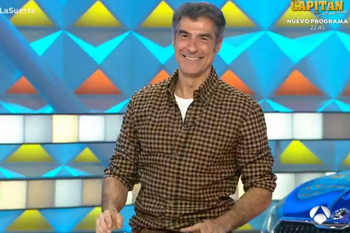 Jorge Fernández sonriente con camisa de cuadros en un set de televisión colorido. Captura de 'La Ruleta de la Suerte' Jorge Fernández sonriente con camisa de cuadros en un set de televisión colorido. Captura de 'La Ruleta de la Suerte'