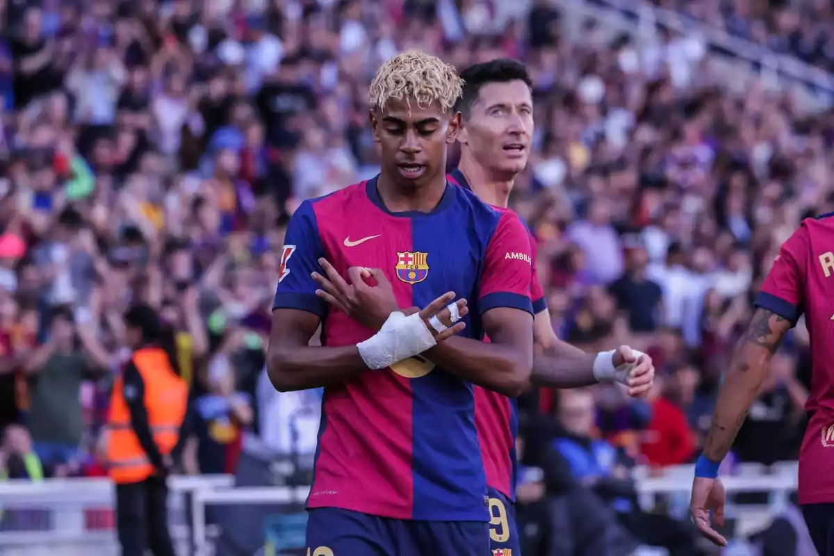 Un jugador de futbol amb l'uniforme del FC Barcelona celebra al camp mentre un altre jugador és darrere d'ell i el públic observa des de les grades. Un jugador de futbol amb l'uniforme del FC Barcelona celebra al camp mentre un altre jugador és darrere d'ell i el públic observa des de les grades.