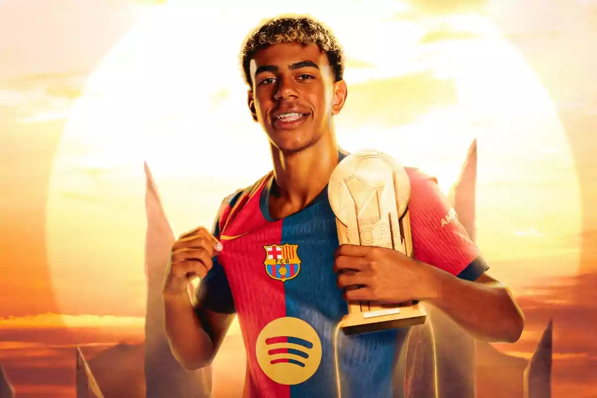 A football player in an FC Barcelona uniform holds a trophy while he smiles at a sunset background.