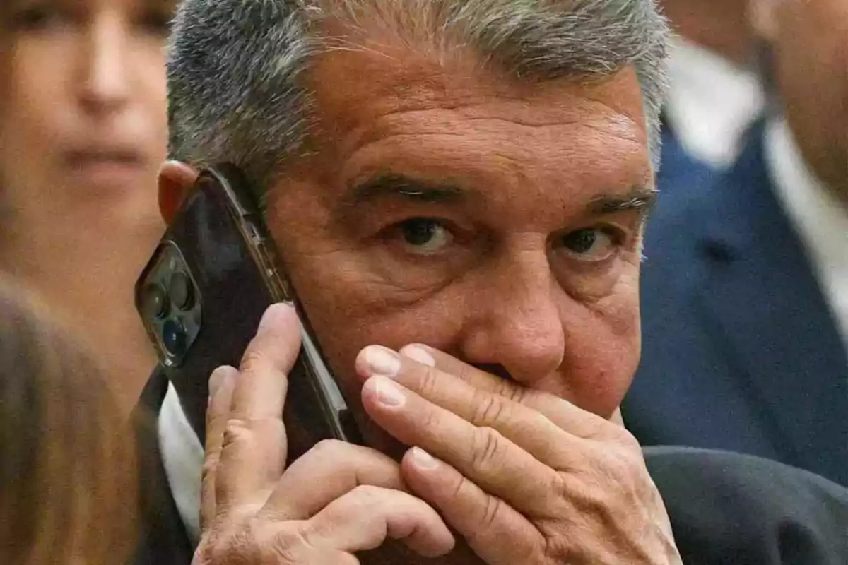 Home de cabell canós parlant per telèfon i cobrint-se la boca amb la mà.