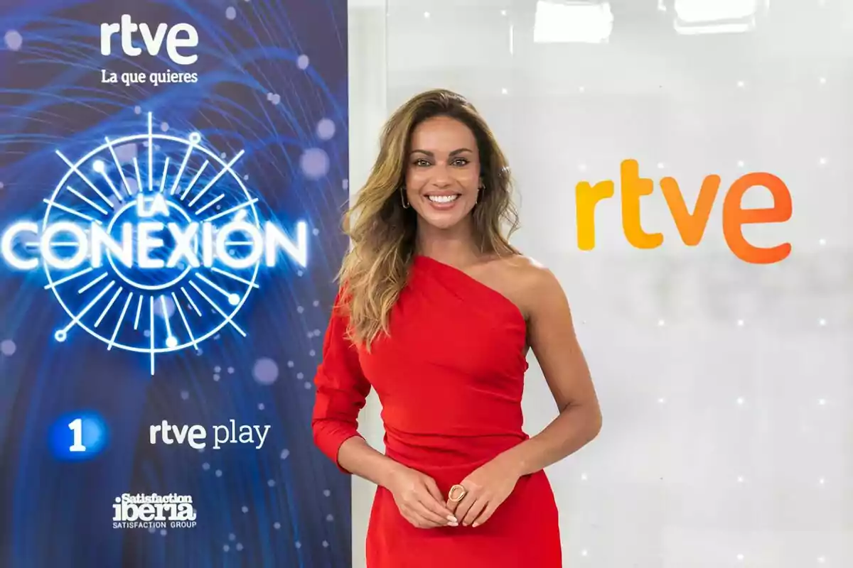 Lara Álvarez amb vestit vermell d’un sol muscle somrient davant d’un fons amb els logotips de RTVE i La Conexió