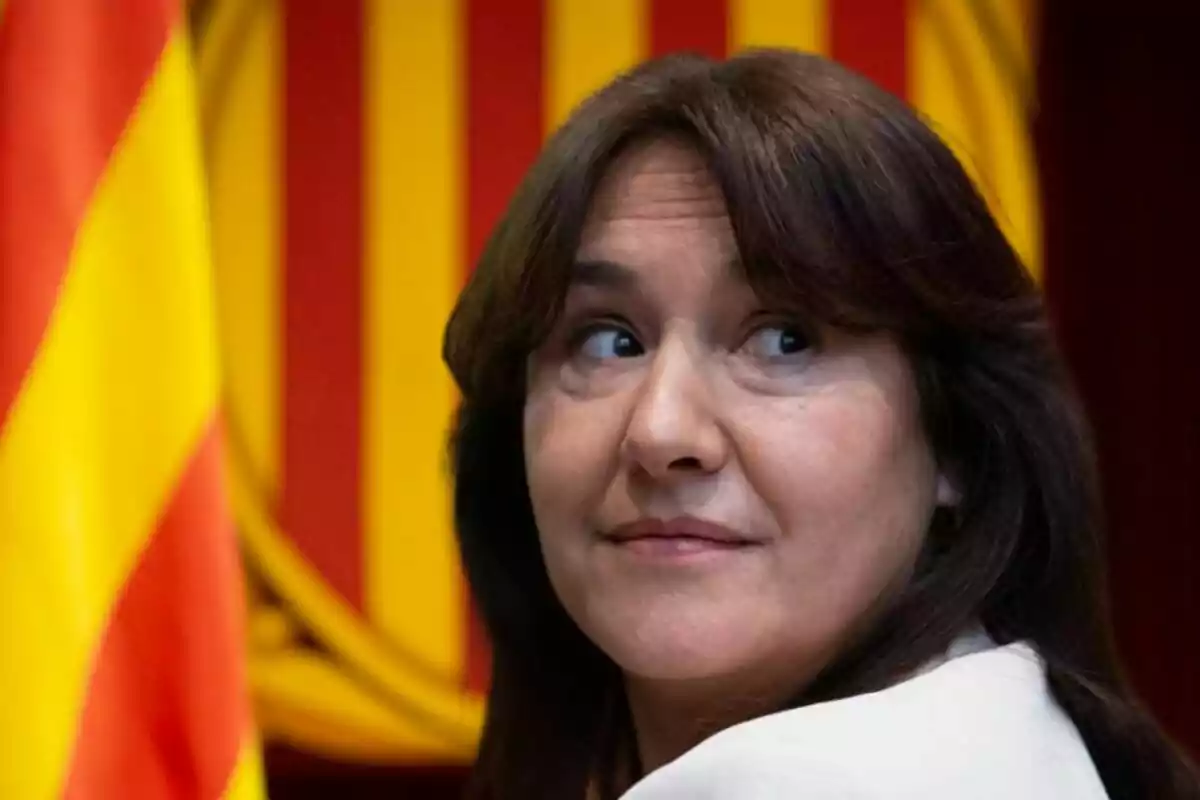 Dona de cabells castanys mira cap a un costat amb una bandera de fons en tons vermells i grocs