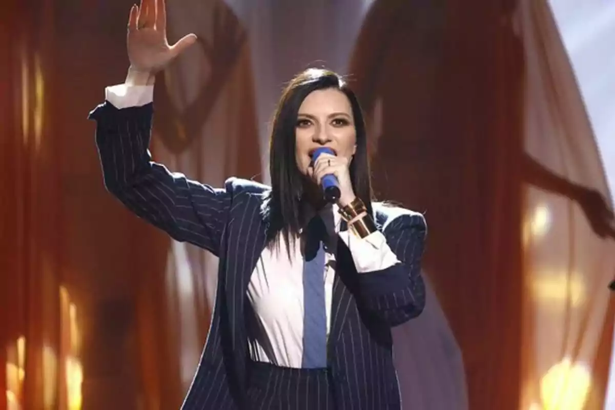 Laura Pausini amb vestit de ratlles canta en un escenari il·luminat mentre aixeca una mà a La Voz.