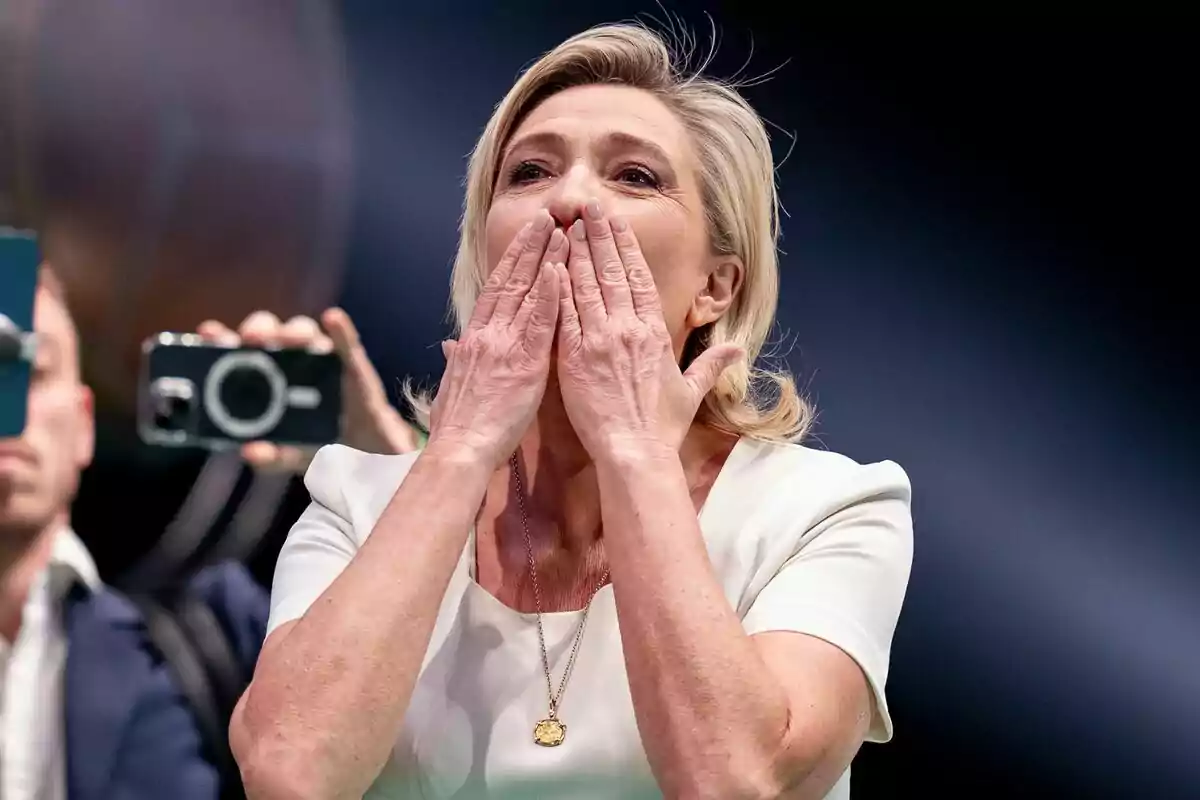 Pla mitjà de Marine Le Pen amb les mans a la boca llançant petons als assistents d'un míting