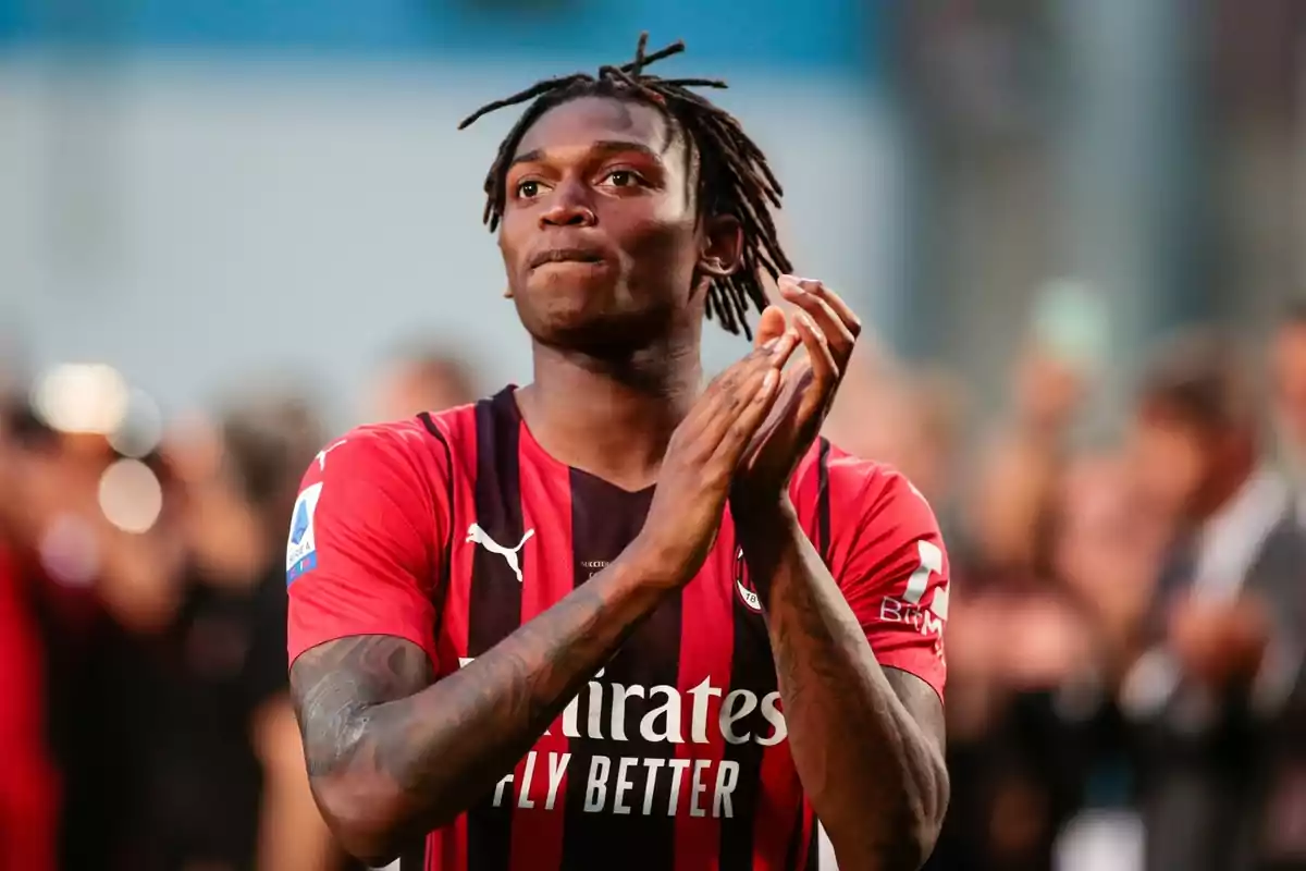 Football player in red and black jersey applauding in a stadium.