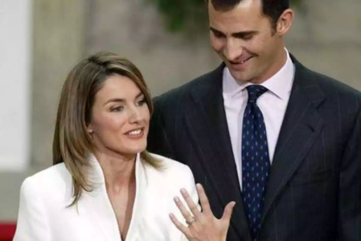 Letizia vestida de blanco enseñando su anillo de compromiso y Felipe riendo con corbata azul y la mirada abajo