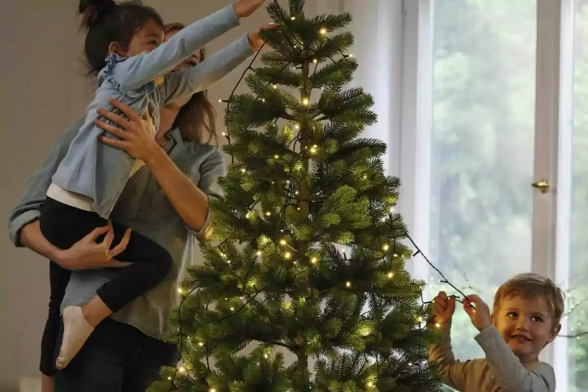 Una familia decorando un árbol de Navidad con luces en una sala iluminada por la luz del día.