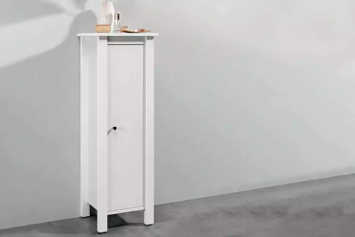 Un moble blanc alt i estret amb una porta i alguns objectes decoratius a la part superior. Un moble blanc alt i estret amb una porta i alguns objectes decoratius a la part superior.