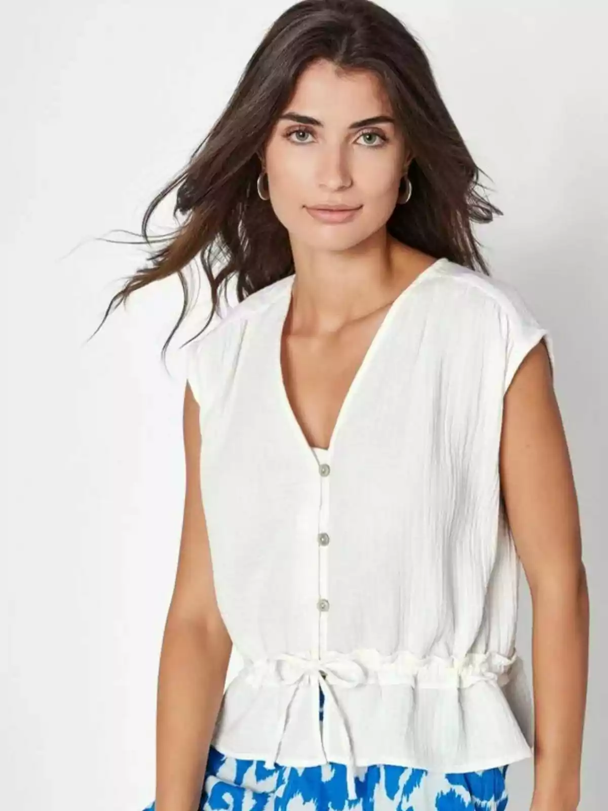 Dona de cabell castany llarg amb una brusa blanca de tirants i uns pantalons blaus amb estampat blanc mirant a la càmera Dona de cabell castany llarg amb una brusa blanca de tirants i uns pantalons blaus amb estampat blanc mirant a la càmera