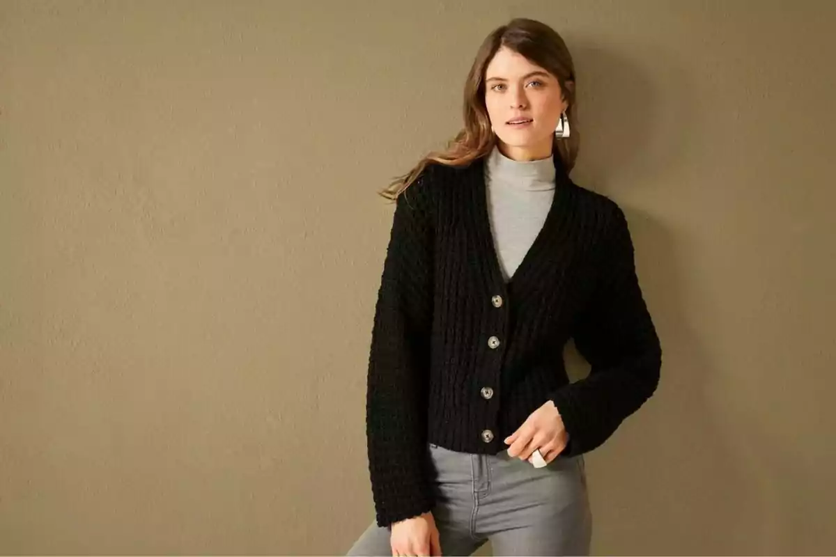 Dona amb suèter negre de punt i pantalons grisos posant davant una paret beix. Dona amb suèter negre de punt i pantalons grisos posant davant una paret beix.