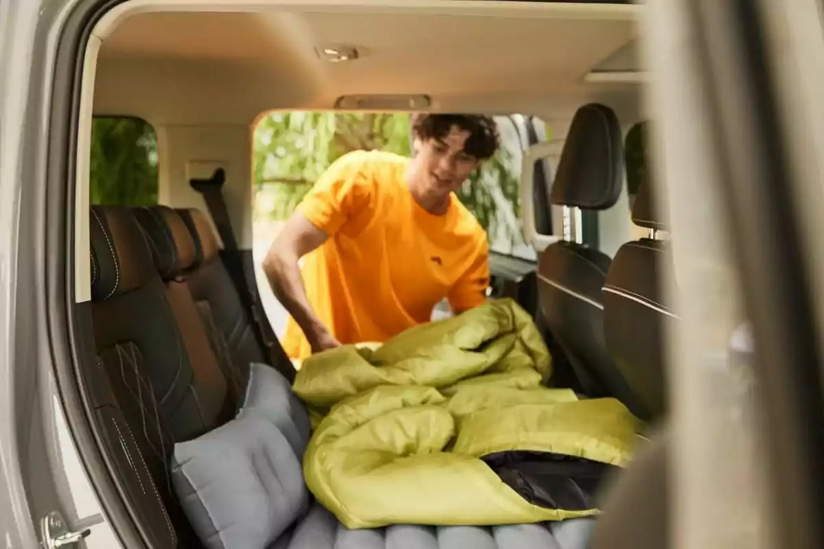Un home amb samarreta taronja col·loca un sac de dormir verd a l'interior d'un vehicle. Un home amb samarreta taronja col·loca un sac de dormir verd a l'interior d'un vehicle.
