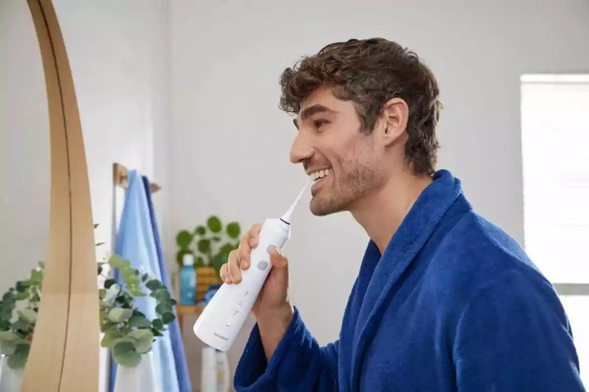 Man using a water flosser in front of the bathroom mirror, wearing a blue robe.