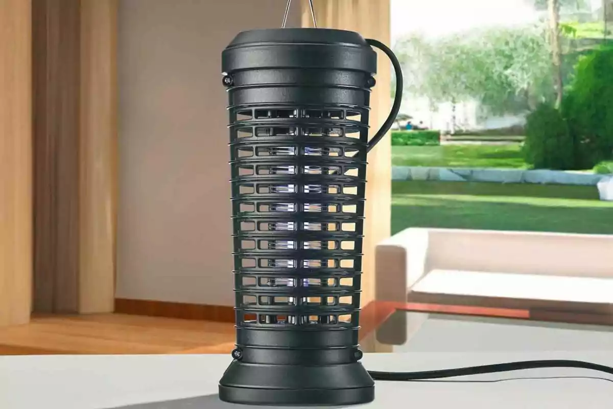 Trampa elèctrica per a insectes de color negre sobre una taula en una sala amb vista al jardí Trampa elèctrica per a insectes de color negre sobre una taula en una sala amb vista al jardí
