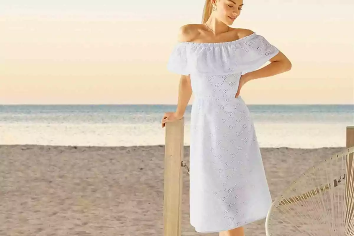 Dona amb vestit blanc de les espatlles descobertes posant a la platja al capvespre Dona amb vestit blanc de les espatlles descobertes posant a la platja al capvespre