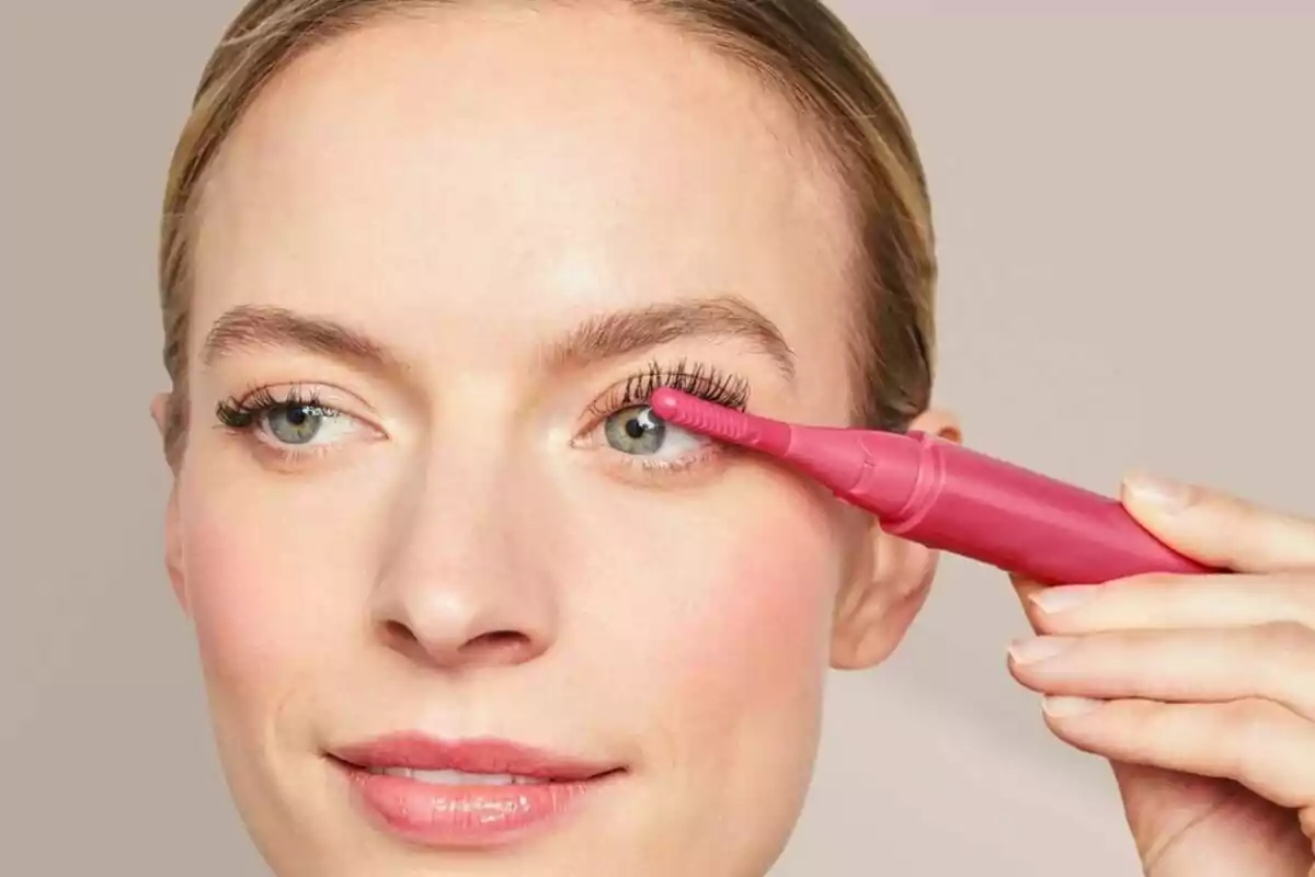 Dona utilitzant un arrissador de pestanyes elèctric rosa al seu ull dret Dona utilitzant un arrissador de pestanyes elèctric rosa al seu ull dret