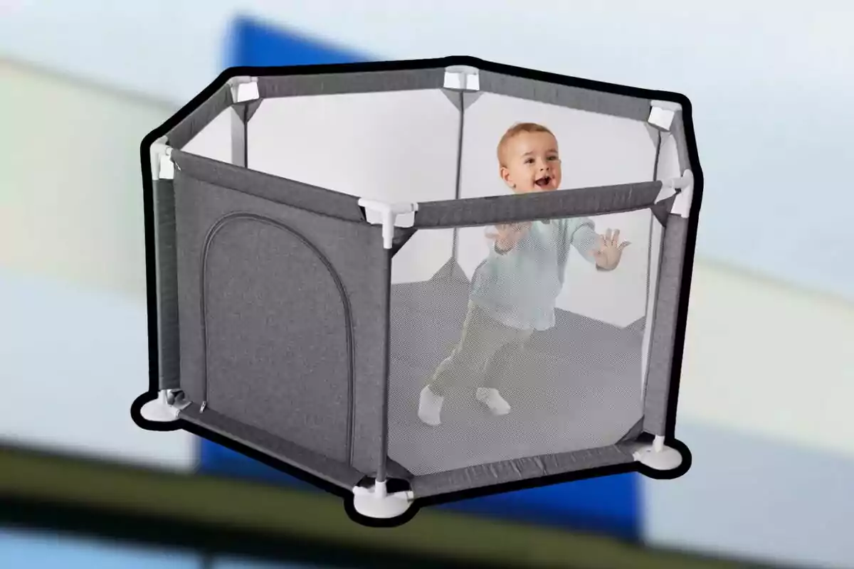 Un bebé sonriente está de pie dentro de un corralito hexagonal de tela gris con malla transparente. Un bebé sonriente está de pie dentro de un corralito hexagonal de tela gris con malla transparente.