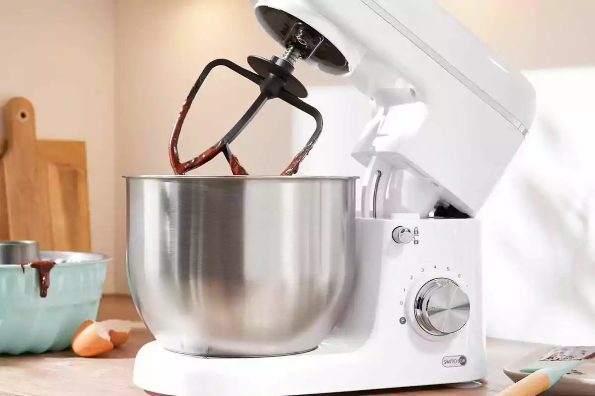 Batidora de pie blanca con un tazón de acero inoxidable y un batidor con mezcla de chocolate en una cocina. Batidora de pie blanca con un tazón de acero inoxidable y un batidor con mezcla de chocolate en una cocina.