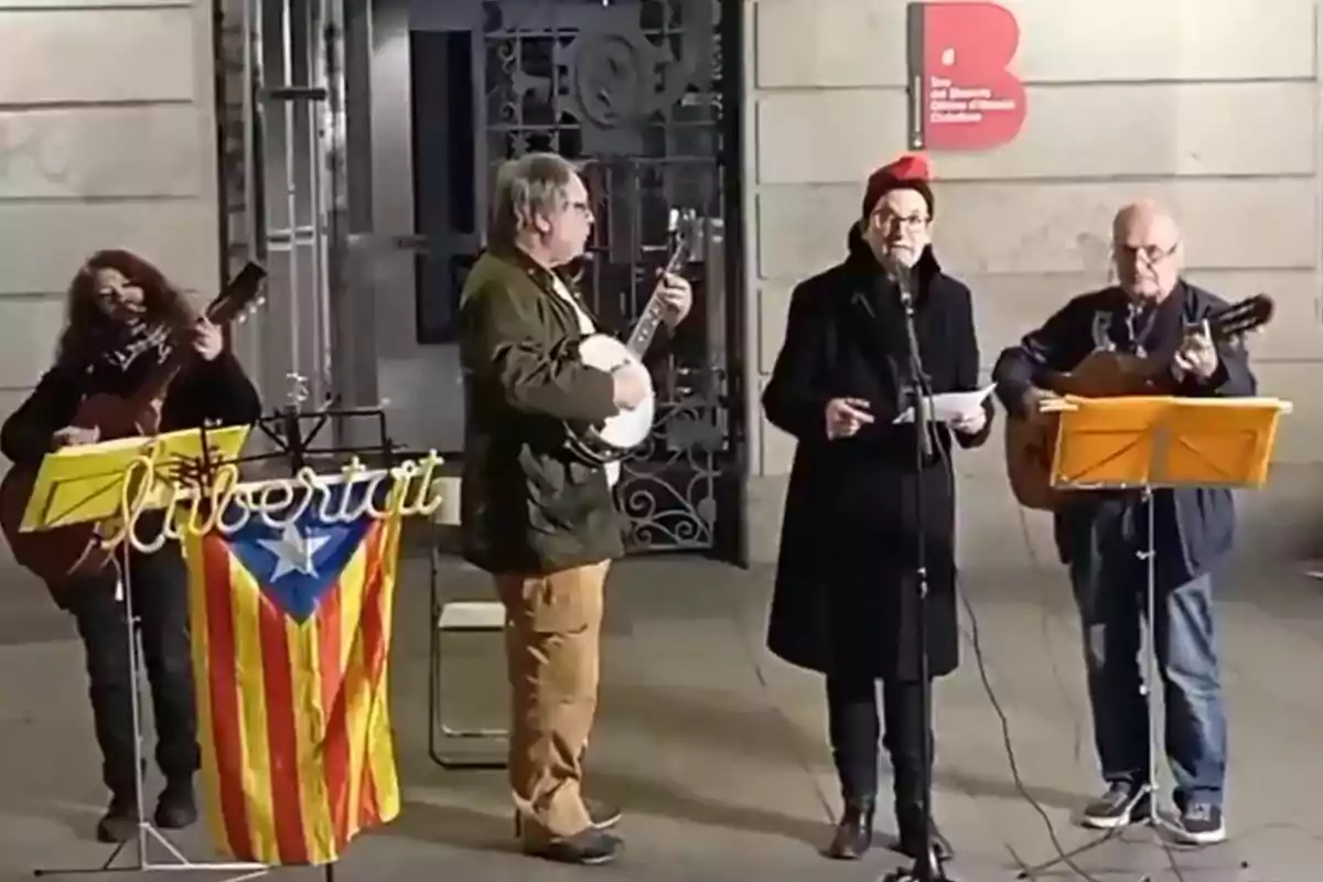 Un grup de persones toca instruments i canta davant d'un edifici, amb una bandera catalana i un cartell que diu “llibertat”.