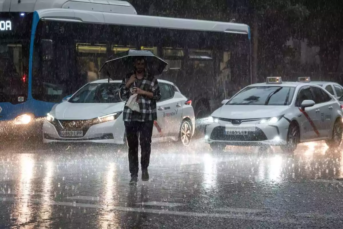 Un home travessant el carrer enmig d'una tempesta i amb cotxes darrere