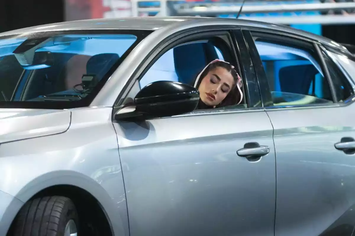 Lola Lolita amb els ulls tancats està asseguda al seient del conductor d'un automòbil platejat a El Desafío. Lola Lolita amb els ulls tancats està asseguda al seient del conductor d'un automòbil platejat a El Desafío.