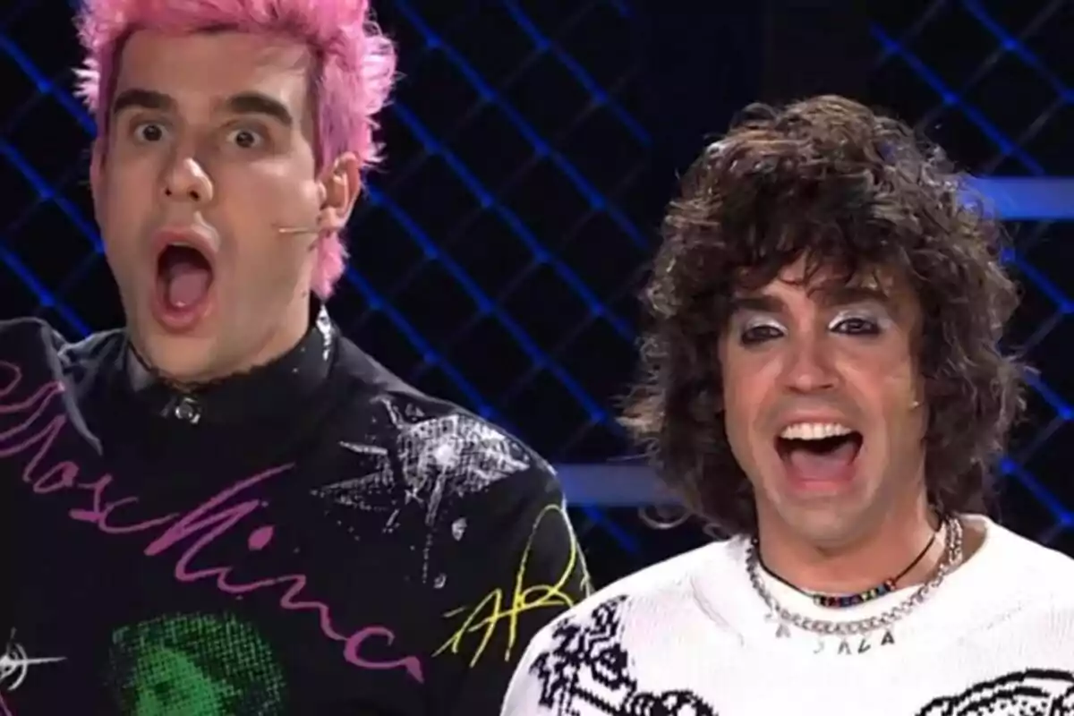 Javi Calvo i Javi Ambrossi amb expressions de sorpresa i alegria, un amb cabell rosat i l'altre amb cabell arrissat, en un escenari il·luminat a Mask Singer.