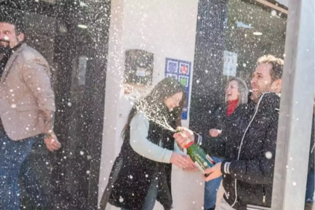 Personas celebrando con una botella de champán que está siendo abierta, con el líquido salpicando a su alrededor.