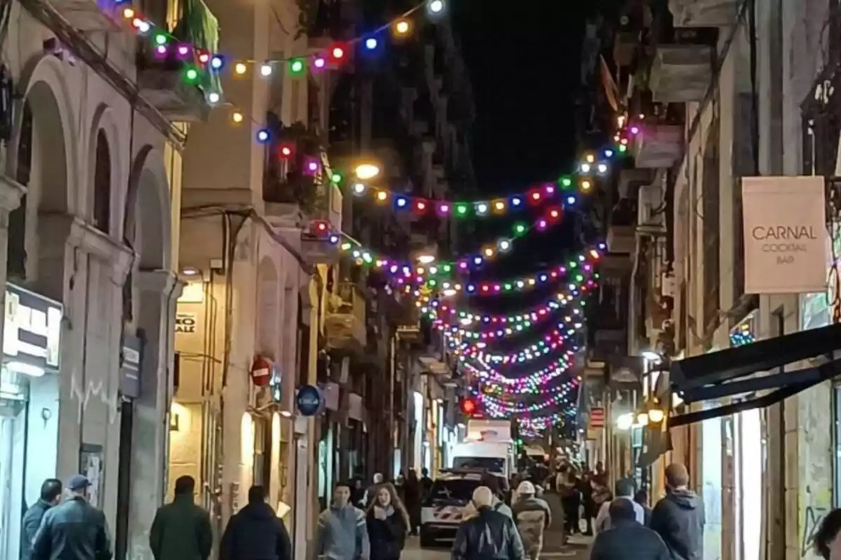 Un carrer il·luminat per llums de colors amb persones caminant per la vorera i edificis a banda i banda.