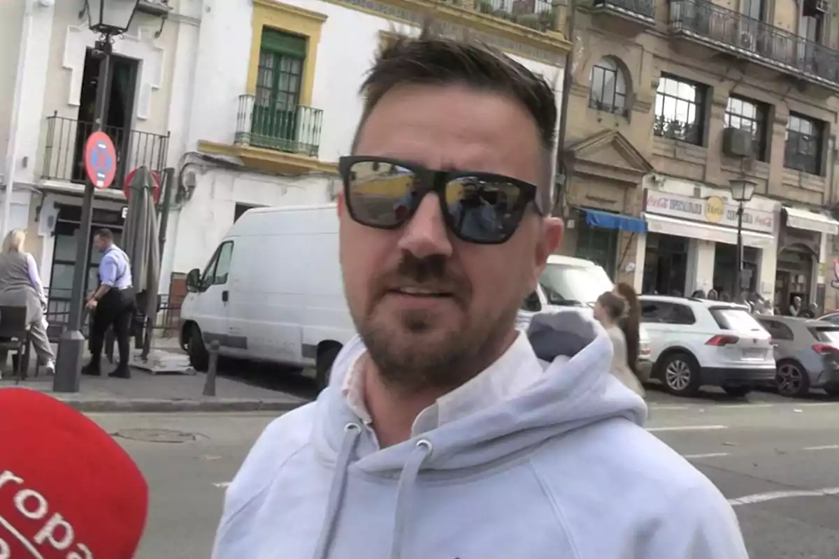 Luis Vicente Rico amb ulleres de sol i dessuadora blanca està en un carrer concorregut amb edificis i cotxes al fons. Luis Vicente Rico amb ulleres de sol i dessuadora blanca està en un carrer concorregut amb edificis i cotxes al fons.